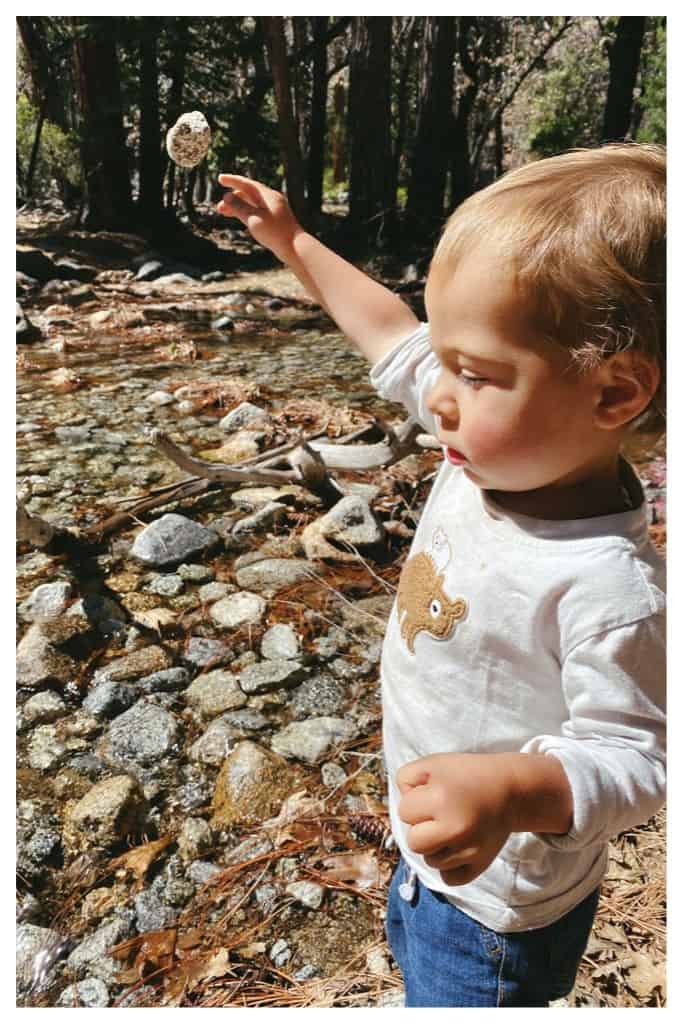 2 year old throwing rocks into a stream while camping